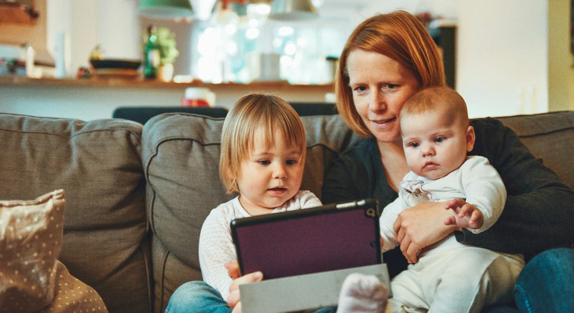 A parent helping two young children use a tablet at home